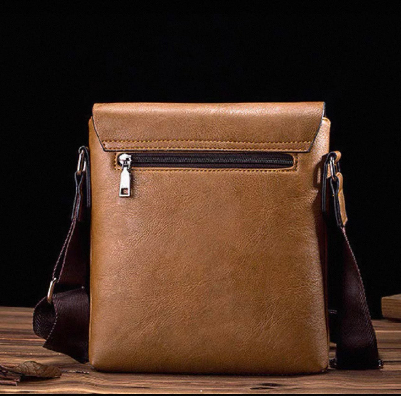 Brown leather crossbody bag on a wooden surface with a dark background