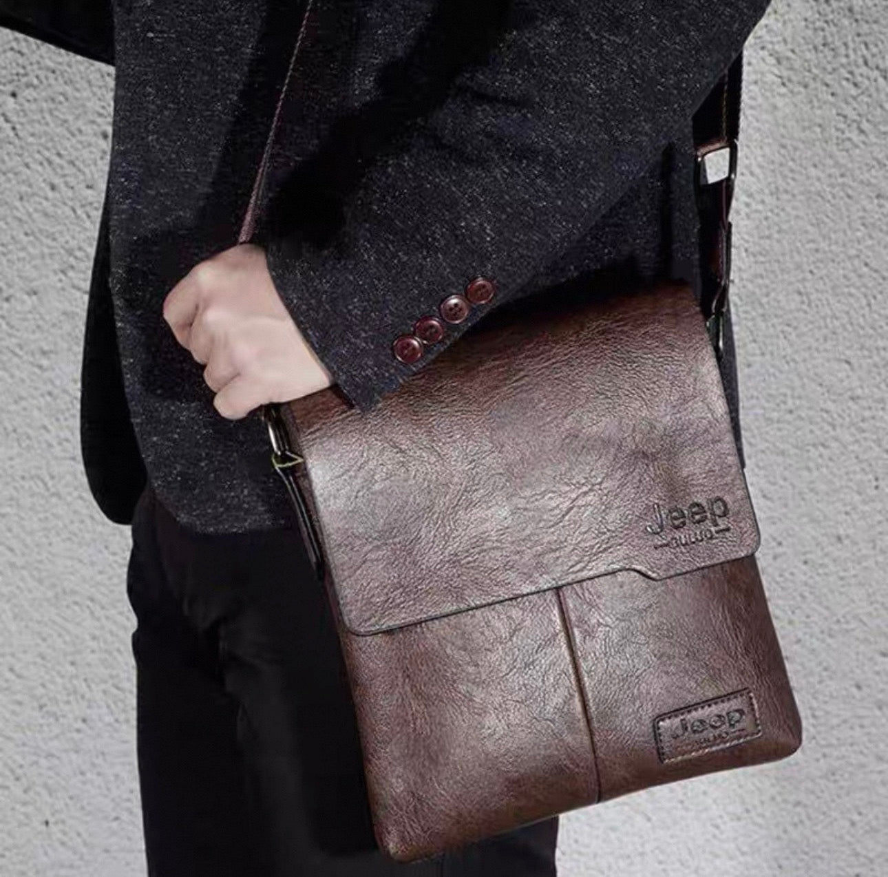 Person holding a brown leather bag with Jeep branding against a gray background