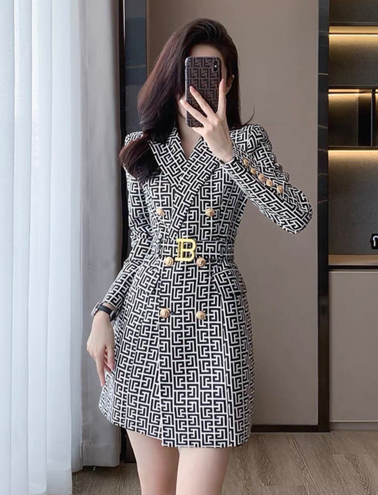 Person wearing a patterned dress with a gold belt in an indoor setting.