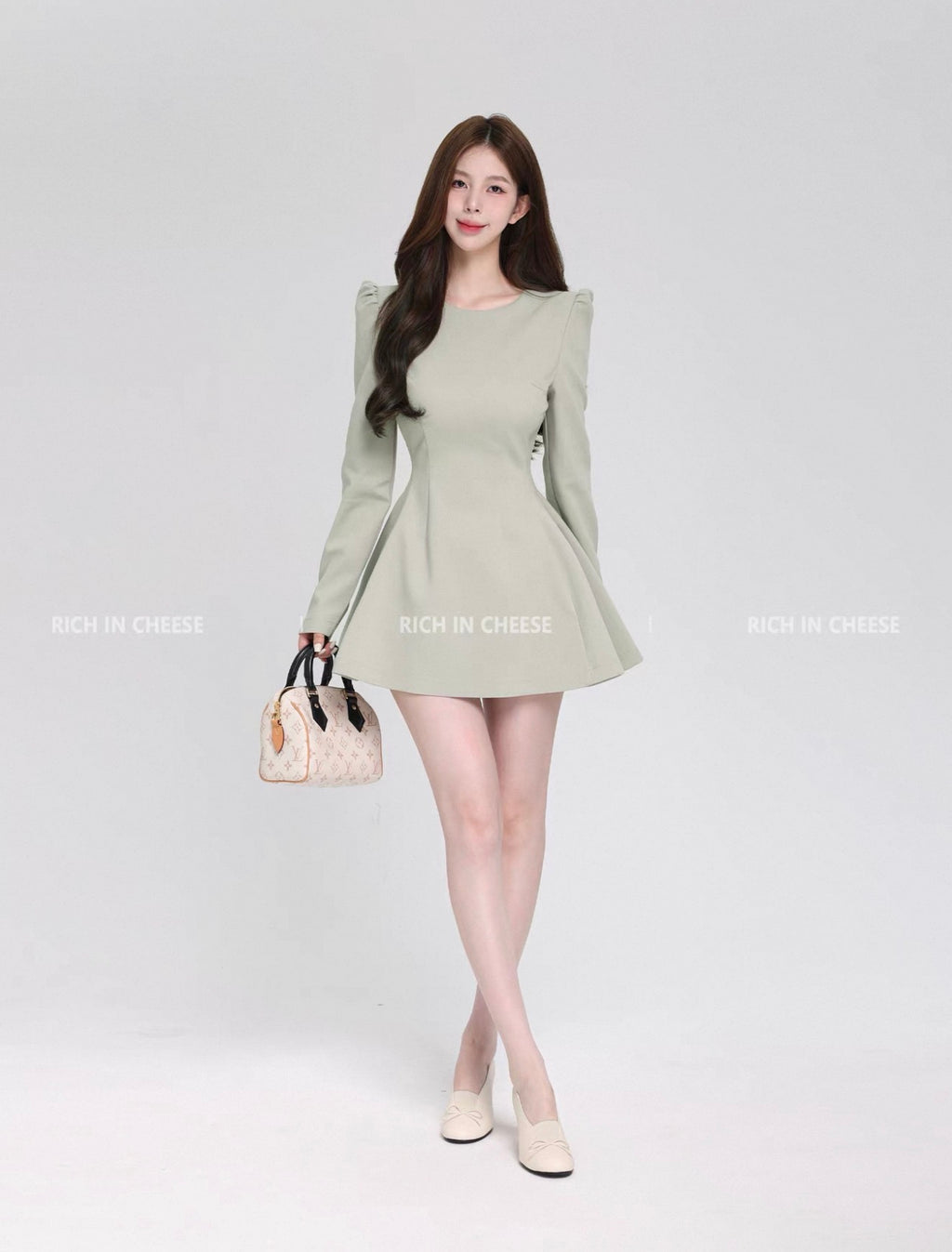 Woman wearing a light green dress holding a handbag on a white background