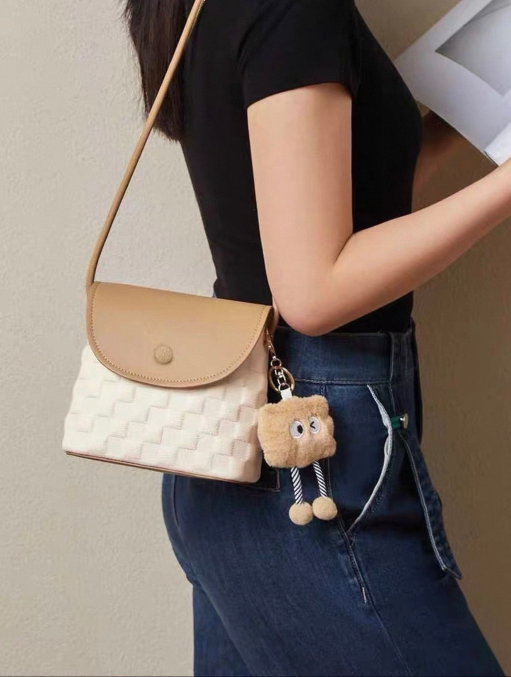 Beige and white small square crossbody bag with flap closure and long strap on model's shoulder.