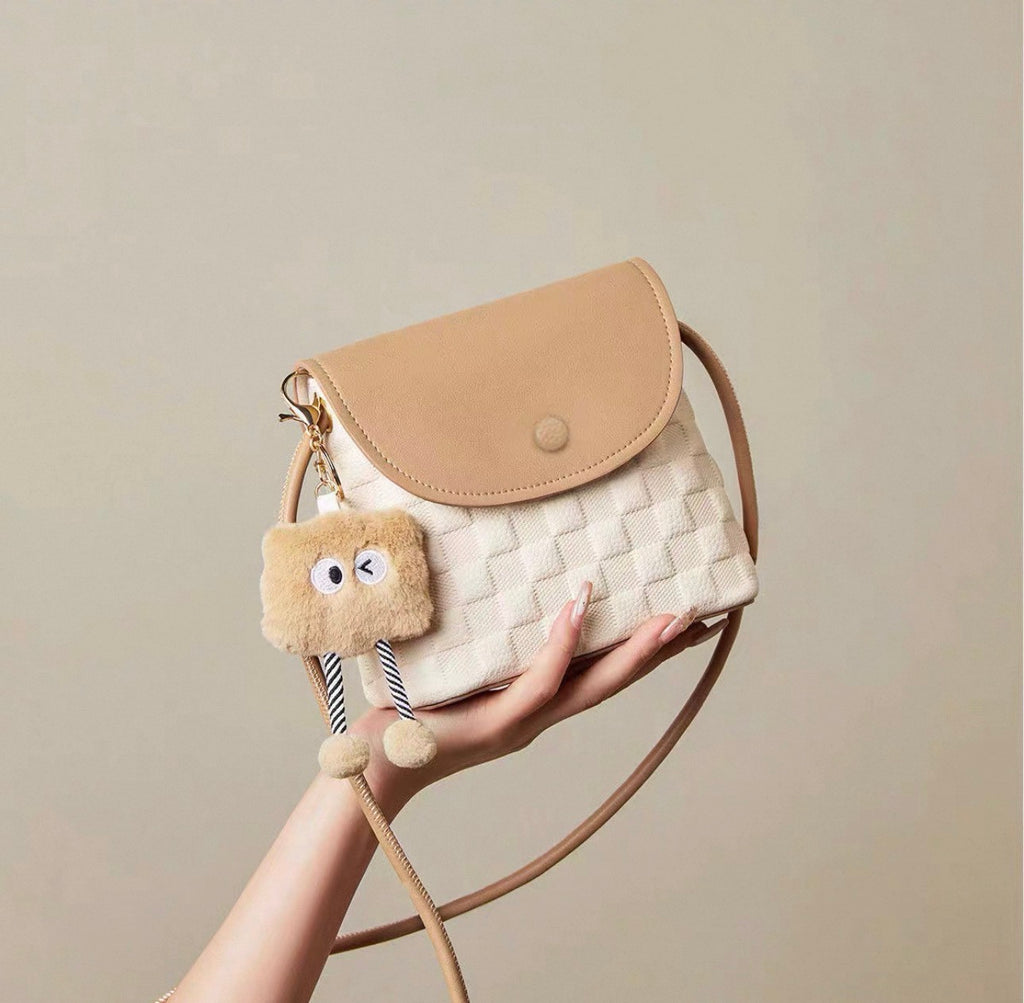 Small square crossbody bag in beige and white with woven texture and plush charm accessory.
