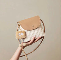 Small square crossbody bag in beige and white with woven texture and plush charm accessory.