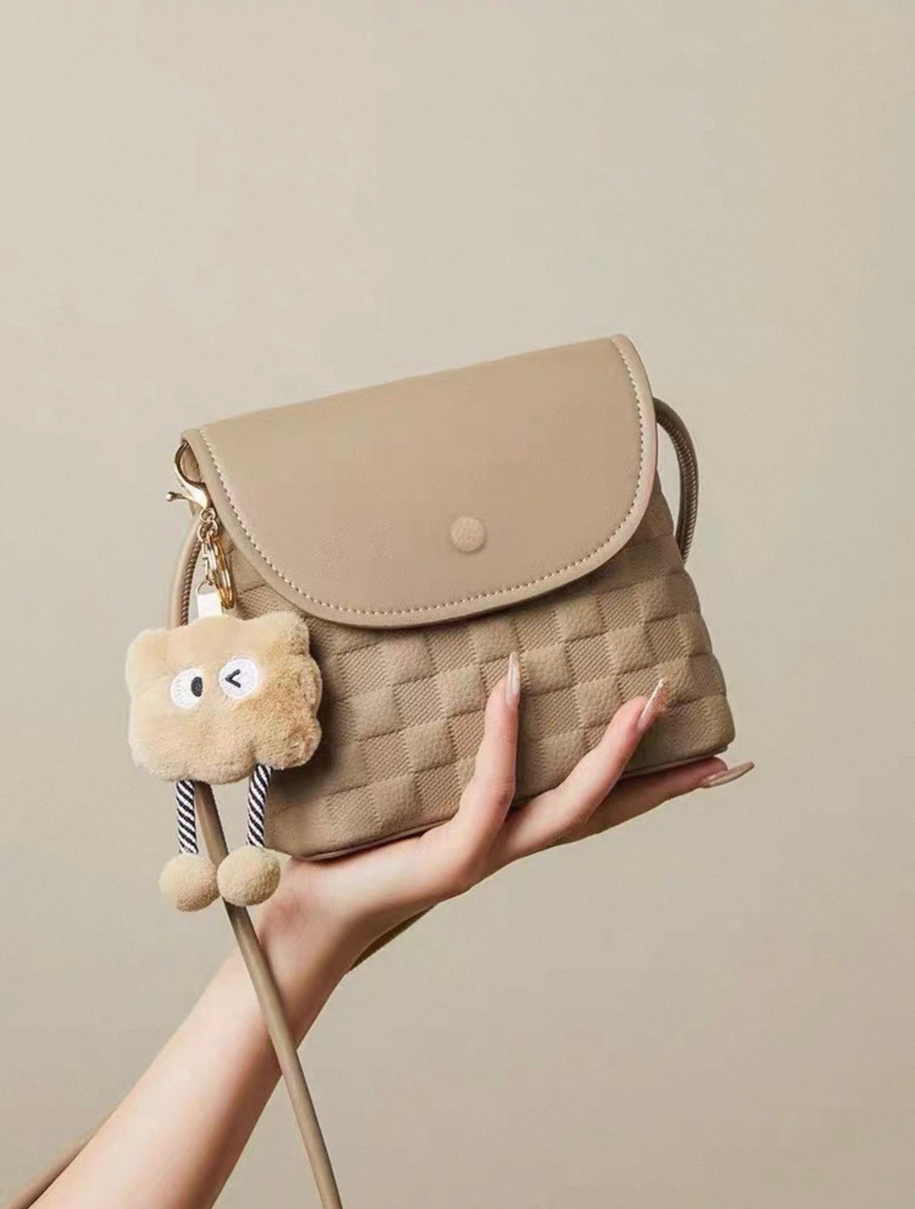 Beige small square crossbody bag with quilted pattern and plush keychain charm.