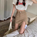 Person wearing a white crop top with red text and beige shorts, standing on a bed.