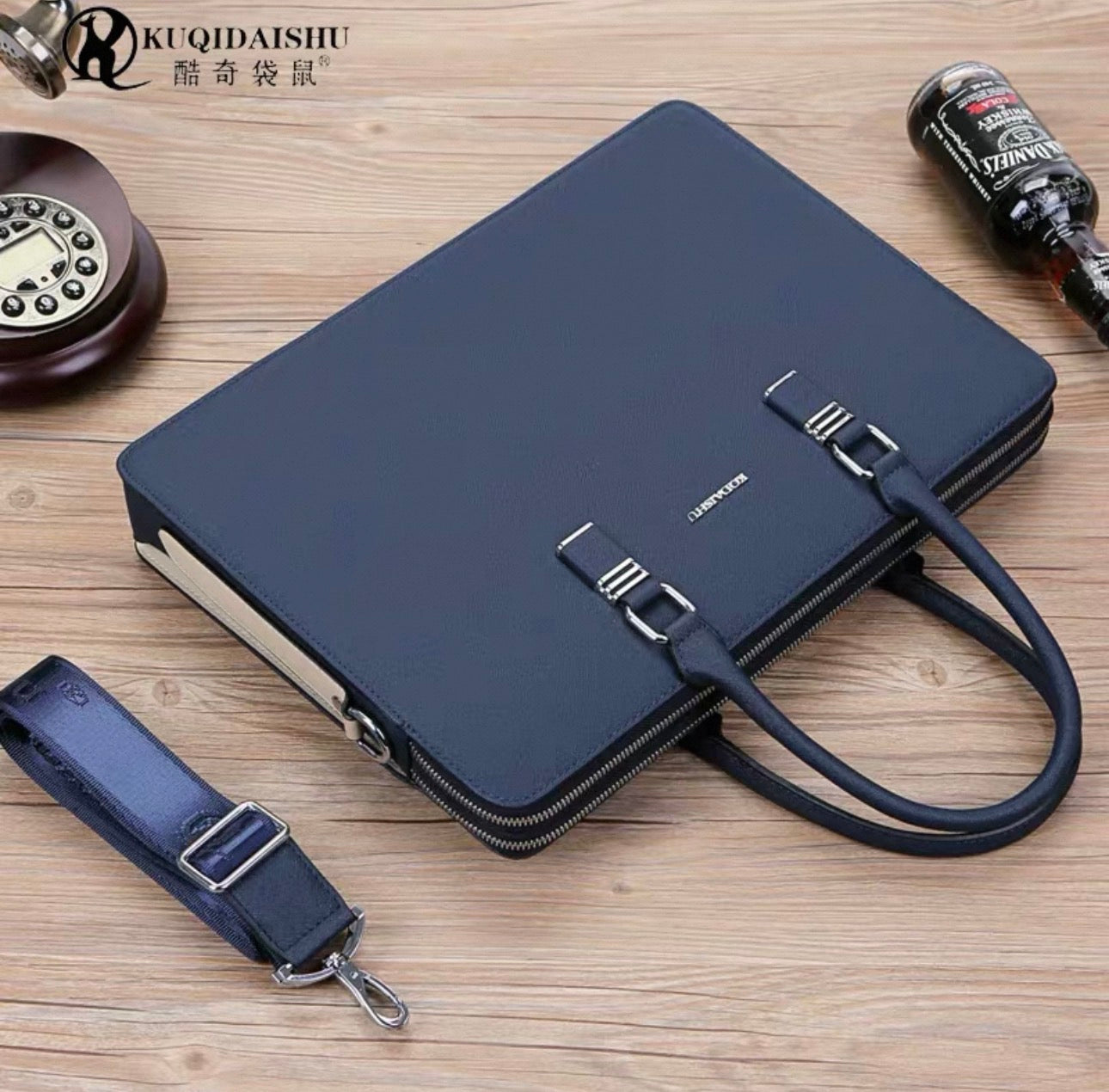 Black briefcase with shoulder strap on a wooden surface, featuring the brand 'KUQIDAISHU'.