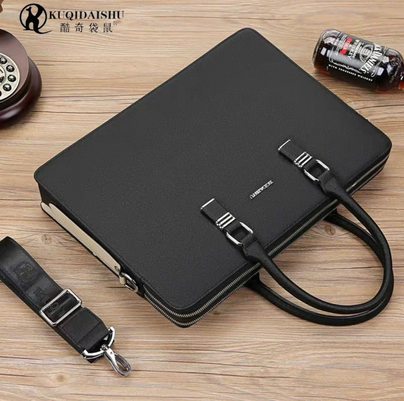 Black briefcase with shoulder strap on a wooden surface, featuring the brand 'KUQIDAISHU'.