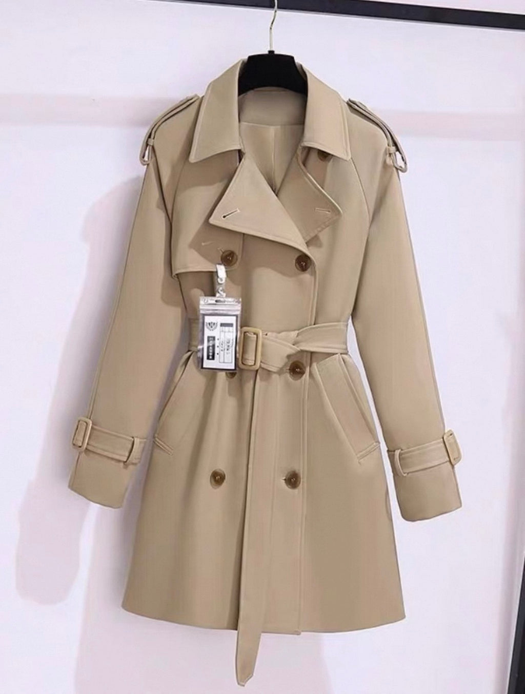 Beige trench coat on a hanger with a white background
