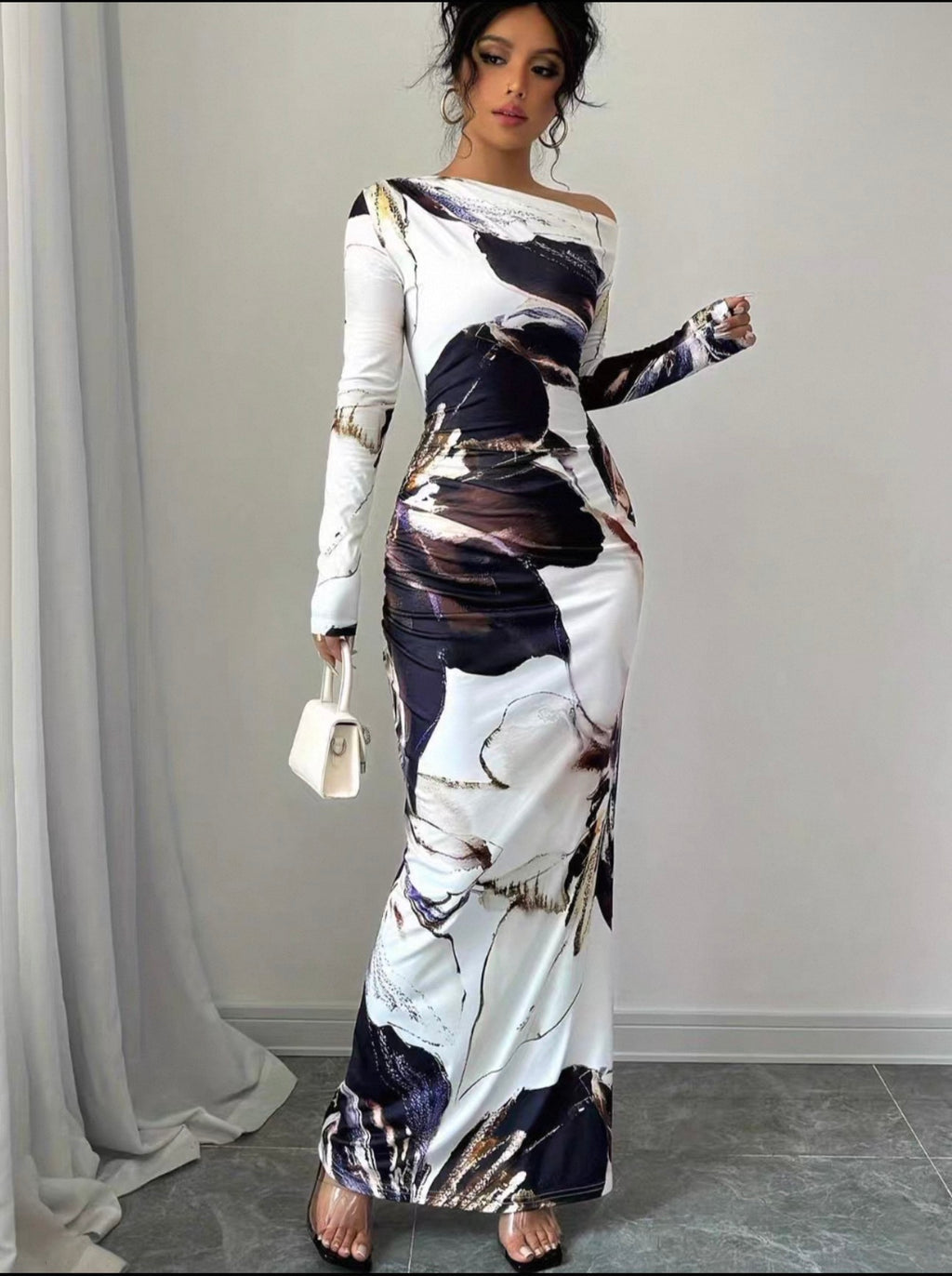 Woman wearing a long, off-shoulder dress with abstract patterns in a room.