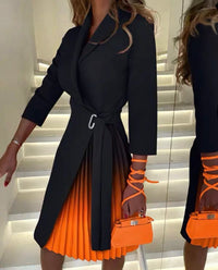 Person wearing a black coat and orange pleated skirt holding an orange handbag.