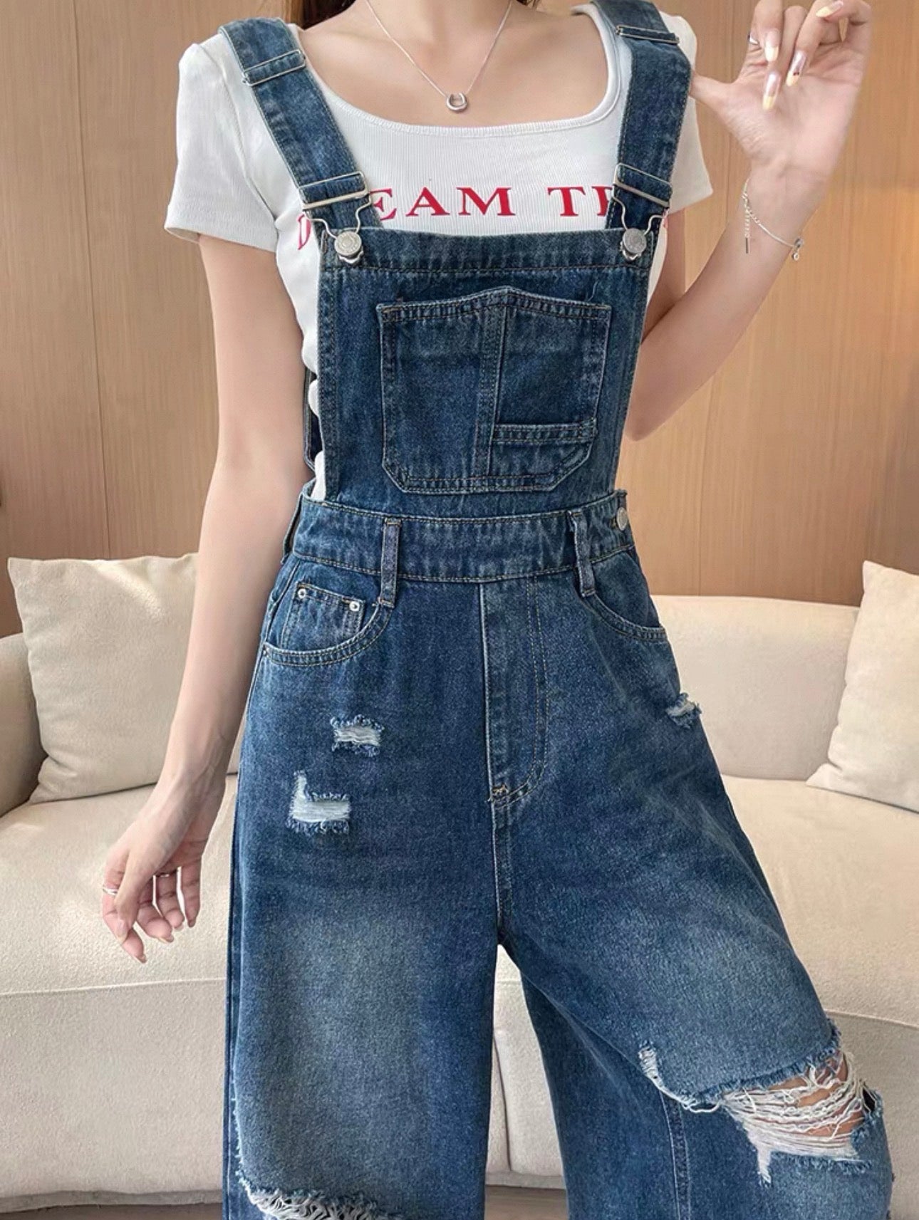 Person wearing a white t-shirt with red text and blue denim overalls in a living room setting.