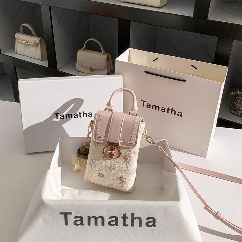Beige handbag with gold accents on a Tamatha branded stand and display box.