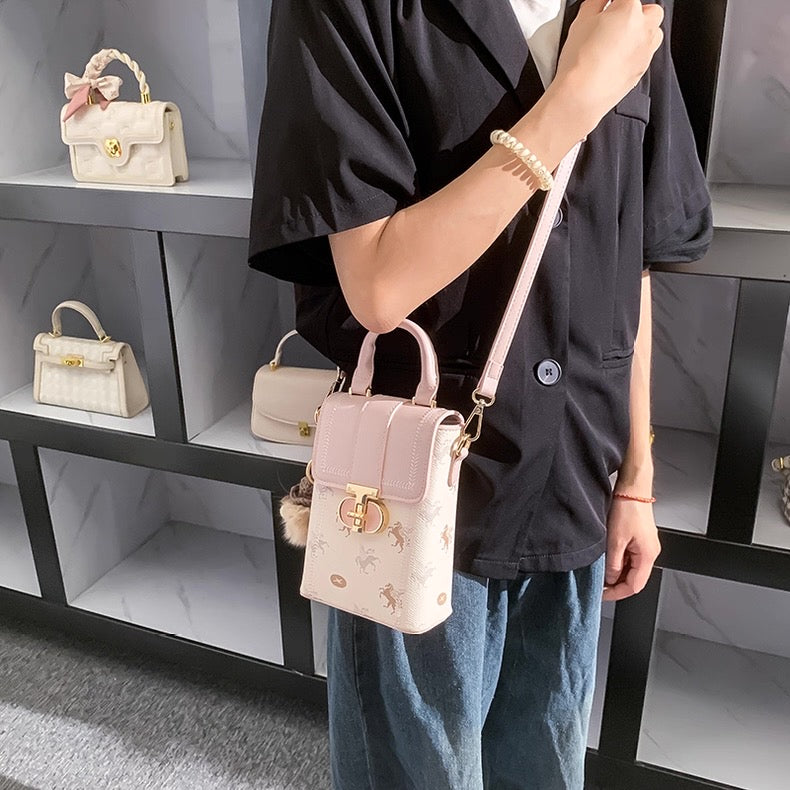 Person holding a light pink handbag with a shelf displaying more handbags in the background.