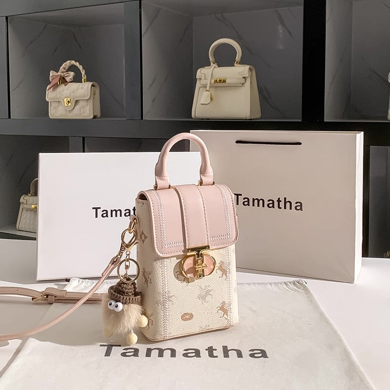 Small handbag with a keychain on a branded surface, with 'Tamatha' branding visible.