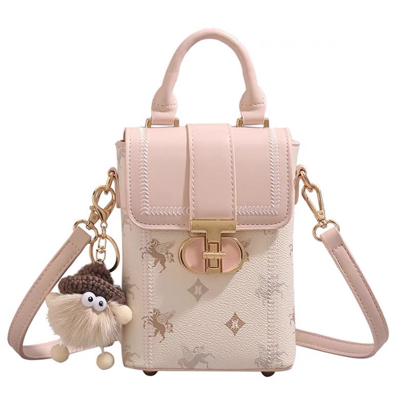 Pink handbag with gold accents and a small plush toy attached on a white background