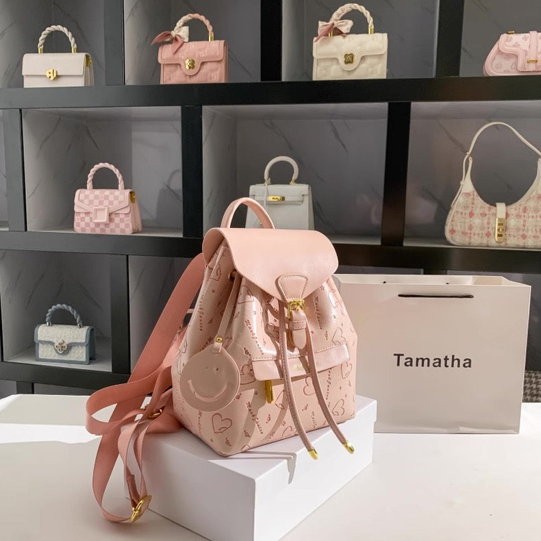 Pink backpack with decorative elements on a white surface, with 'Tamatha' brand box in the background.