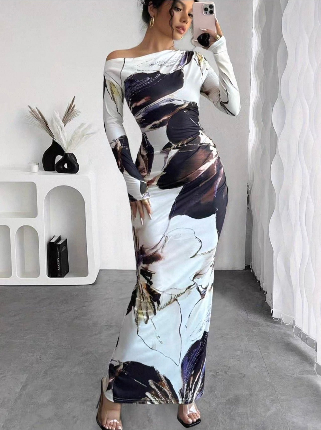 Woman wearing a long, off-shoulder dress with abstract pattern in a minimalistic room.
