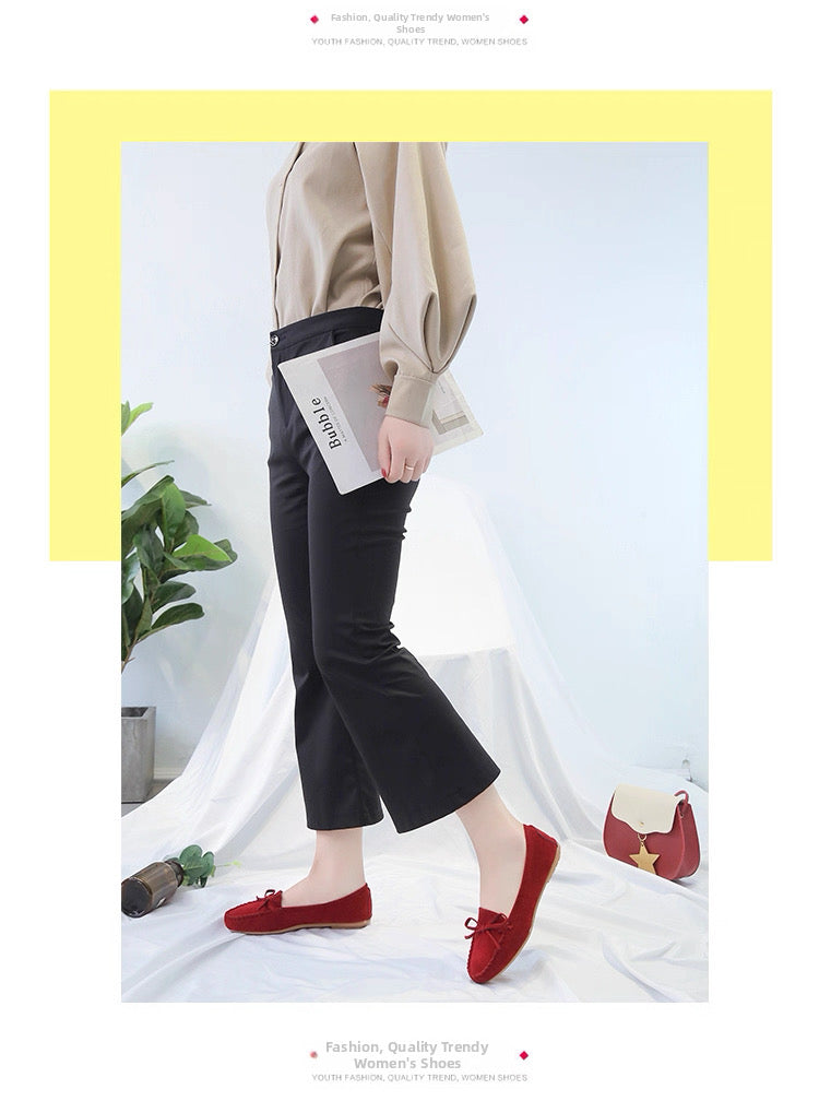 Person wearing black pants and red shoes in a minimalistic setting with a plant and bag.