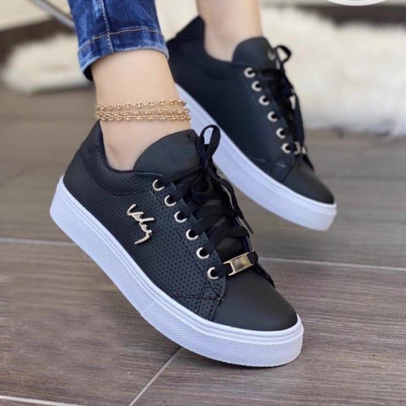 Black sneakers with white soles worn by a person on a wooden floor.