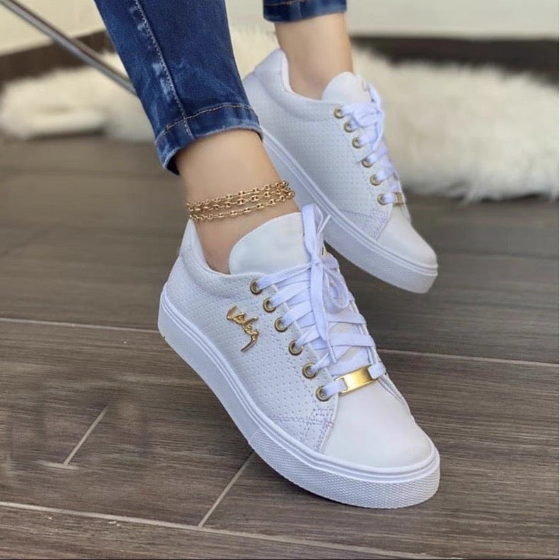 White sneakers with gold accents worn by a person on a wooden floor.