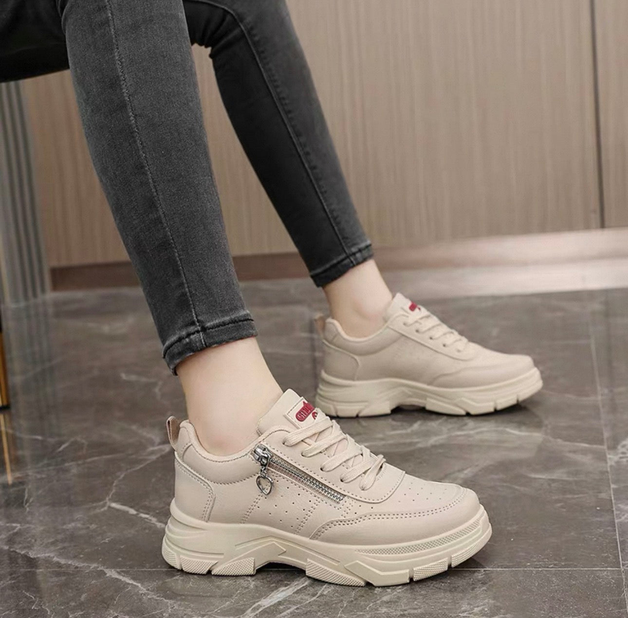 Beige sneakers worn with black pants on a marble floor.