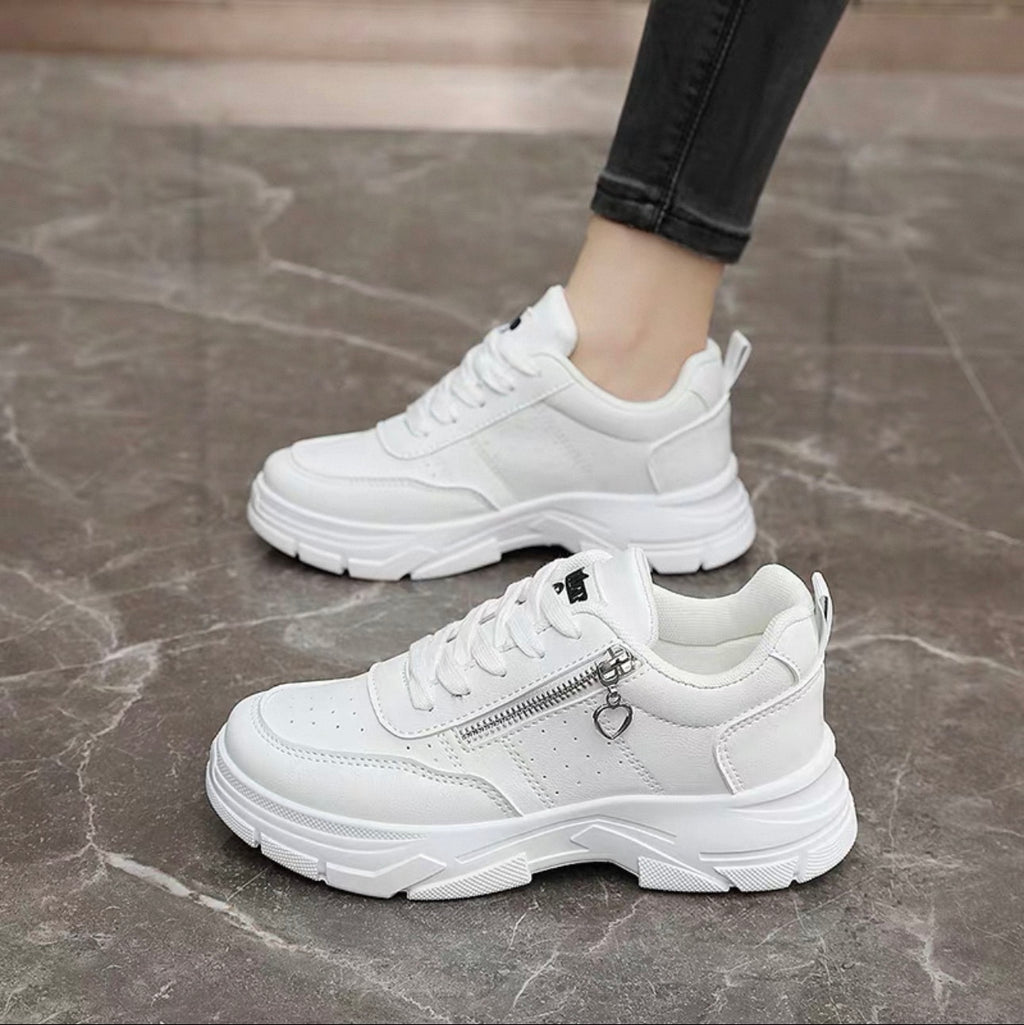 White sneakers with a heart-shaped zipper on a gray floor.