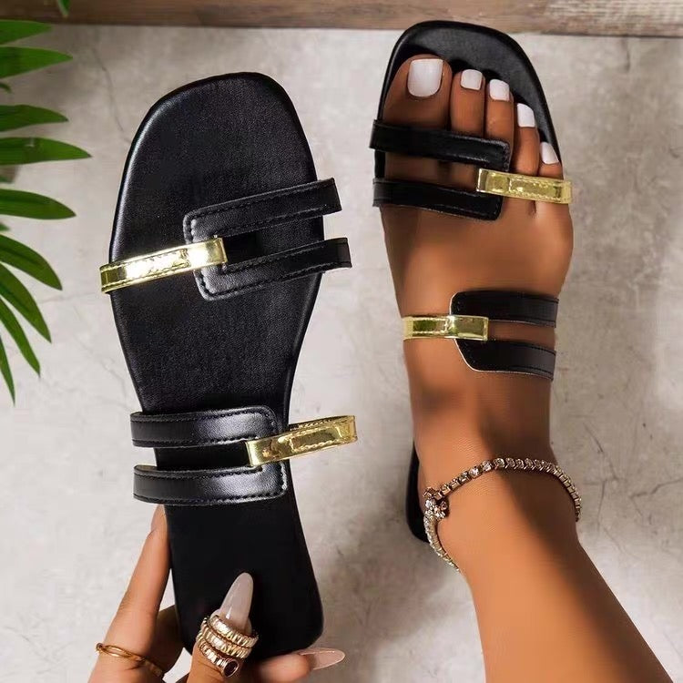 Black sandals with gold accents worn by a person on a neutral background