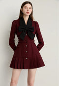 Woman wearing a burgundy outfit with a black bow tie on a plain background