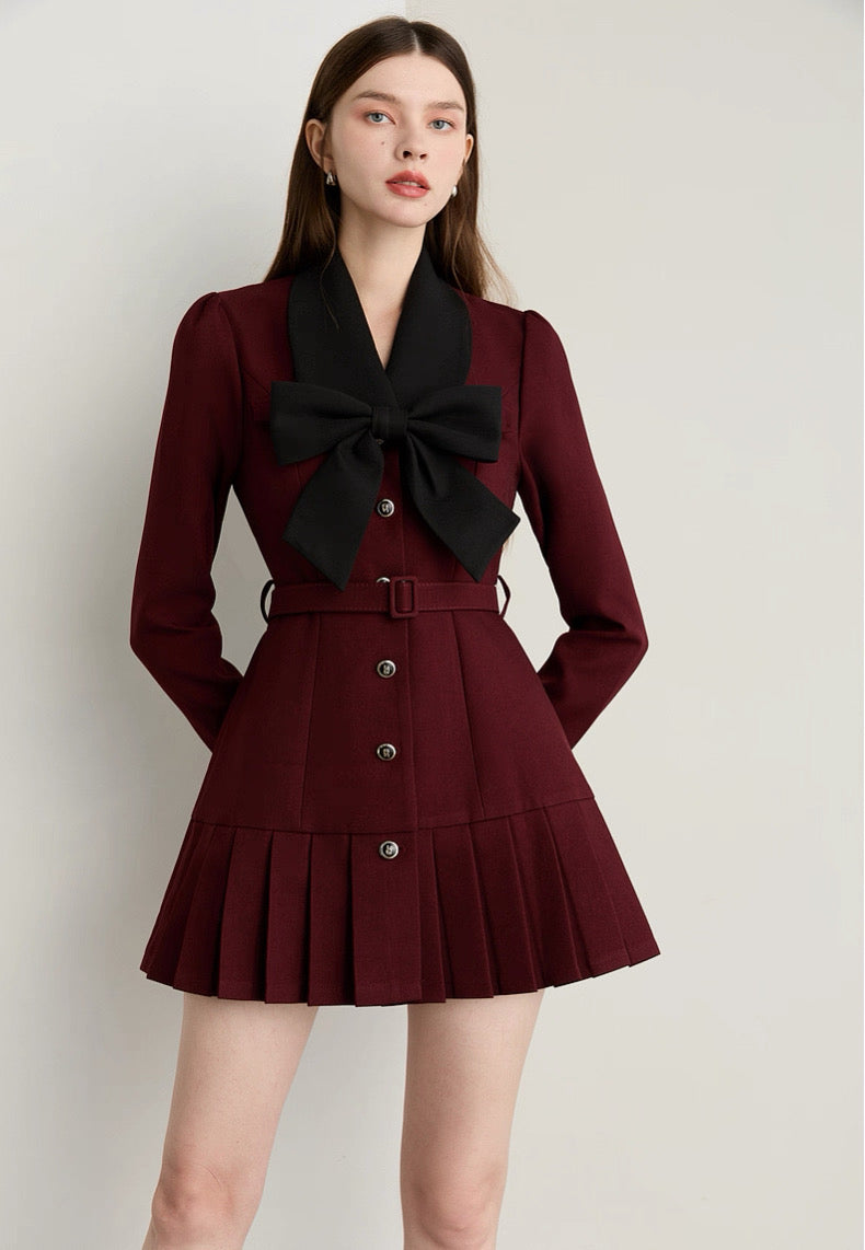 Woman wearing a burgundy outfit with a black bow tie on a plain background