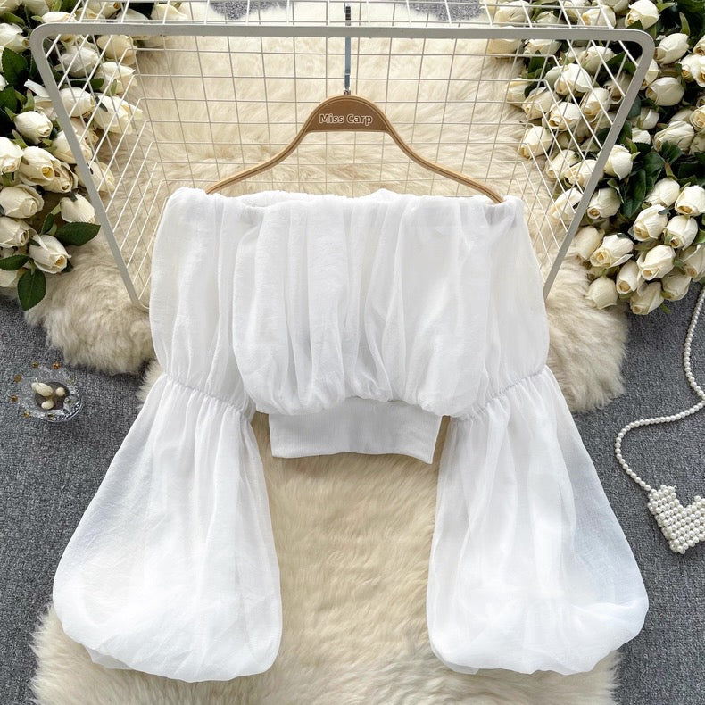White blouse with ruffled sleeves on a hanger against a decorative background with flowers and fur.