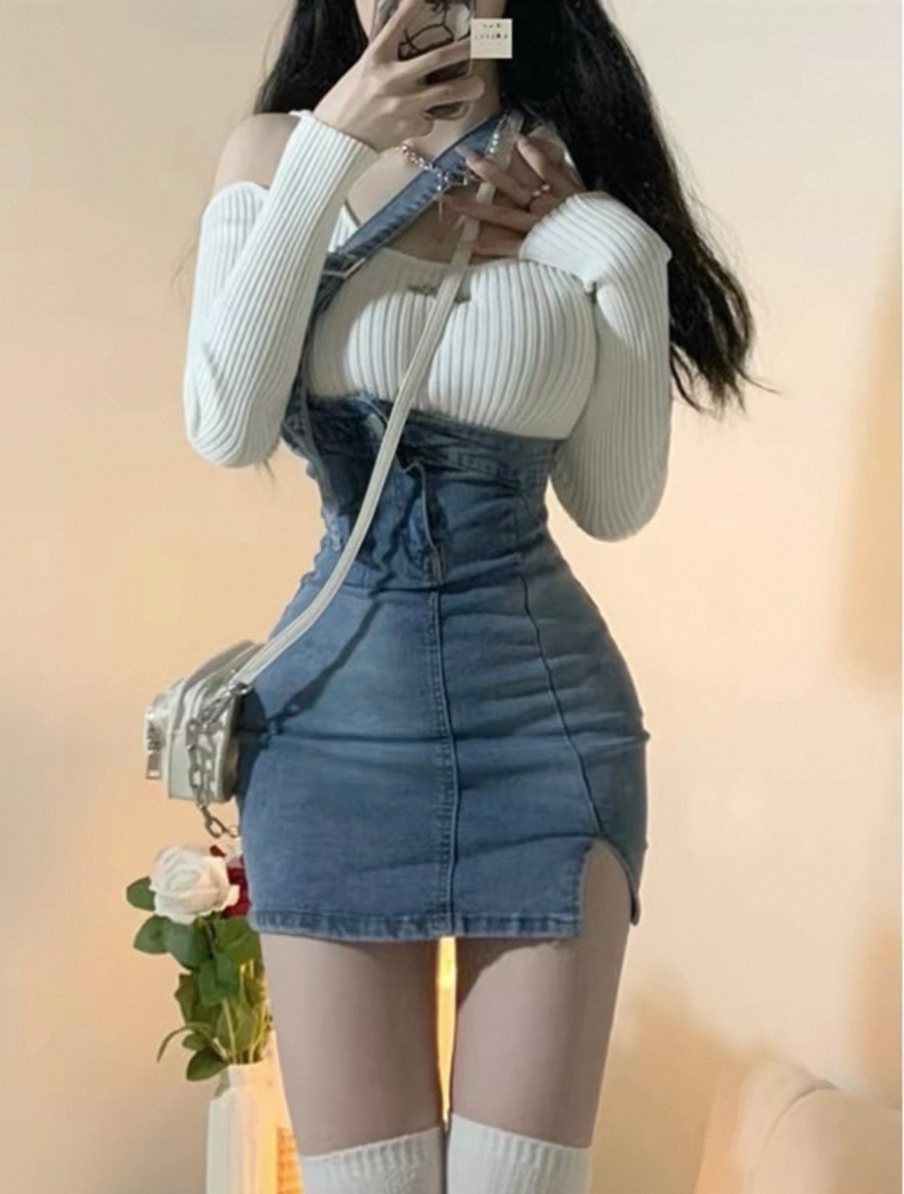 Person wearing a white ribbed sweater and denim skirt with a blurred background