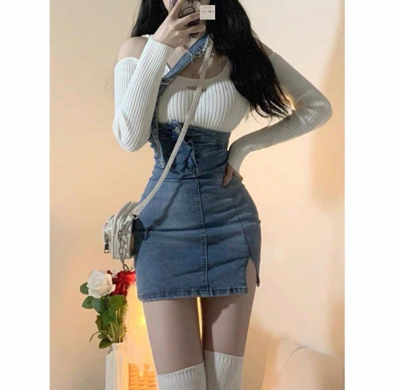 Person wearing a white off-shoulder top and blue denim overalls against a beige background.