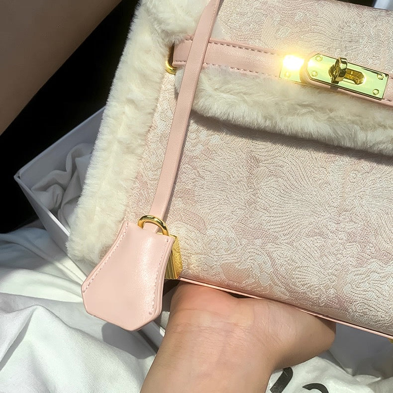Light pink Kelly-style bag with subtle floral embroidery, gold hardware, and soft fringe details.