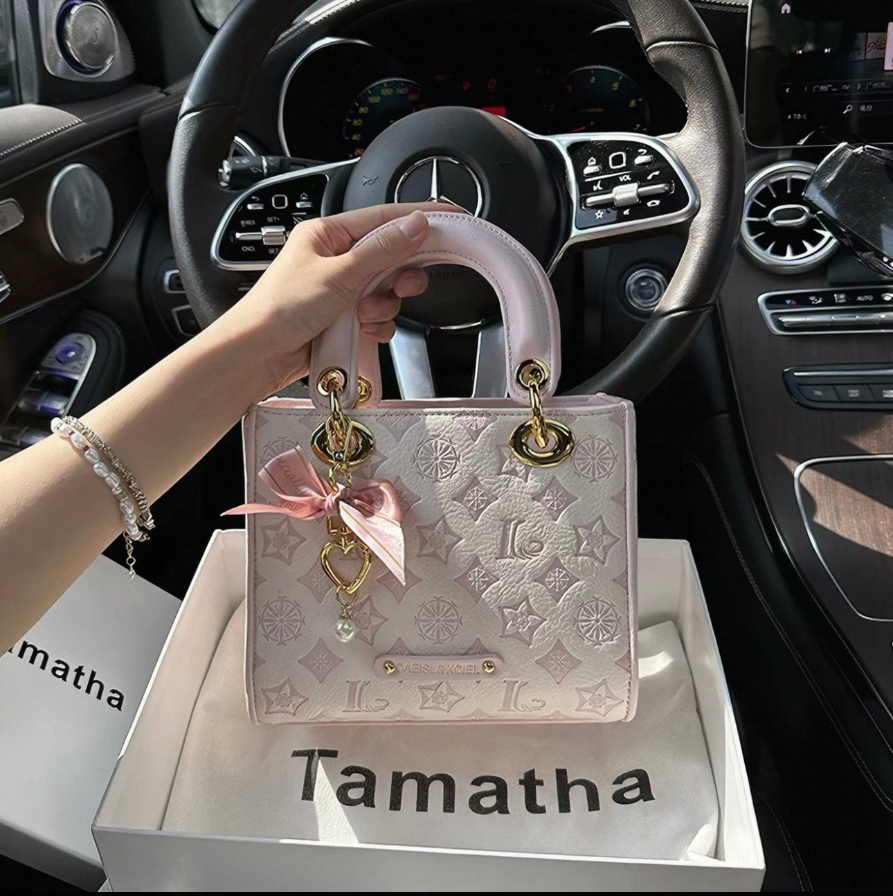 Light pink embossed leather handbag with gold hardware and a satin bow charm.