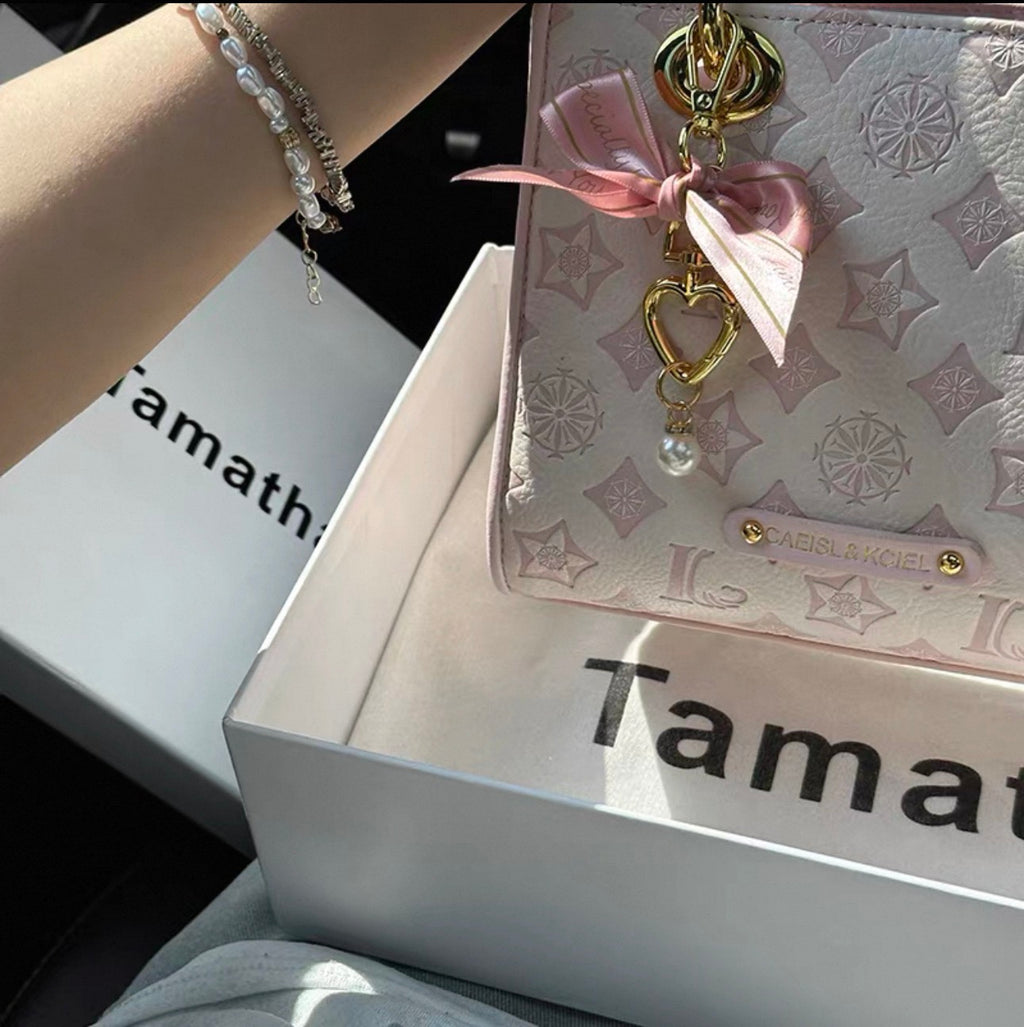 Light pink embossed leather crossbody bag with gold heart charm and pink ribbon bow detailing.