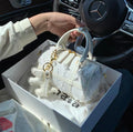 White structured Boston handbag with snowflake pattern and tassel charm on gold hardware.