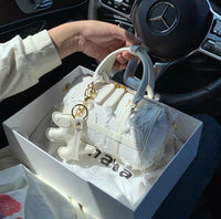 White structured Boston handbag with snowflake pattern and tassel charm on gold hardware.