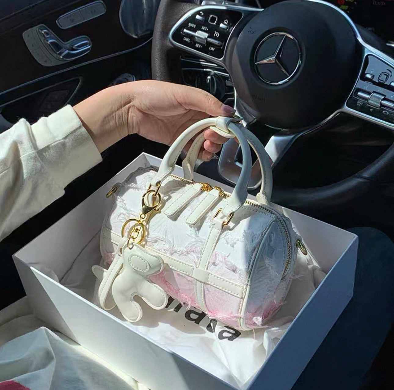 White Boston handbag with snowflake tassel and gold-tone charms, transparent-panel design.