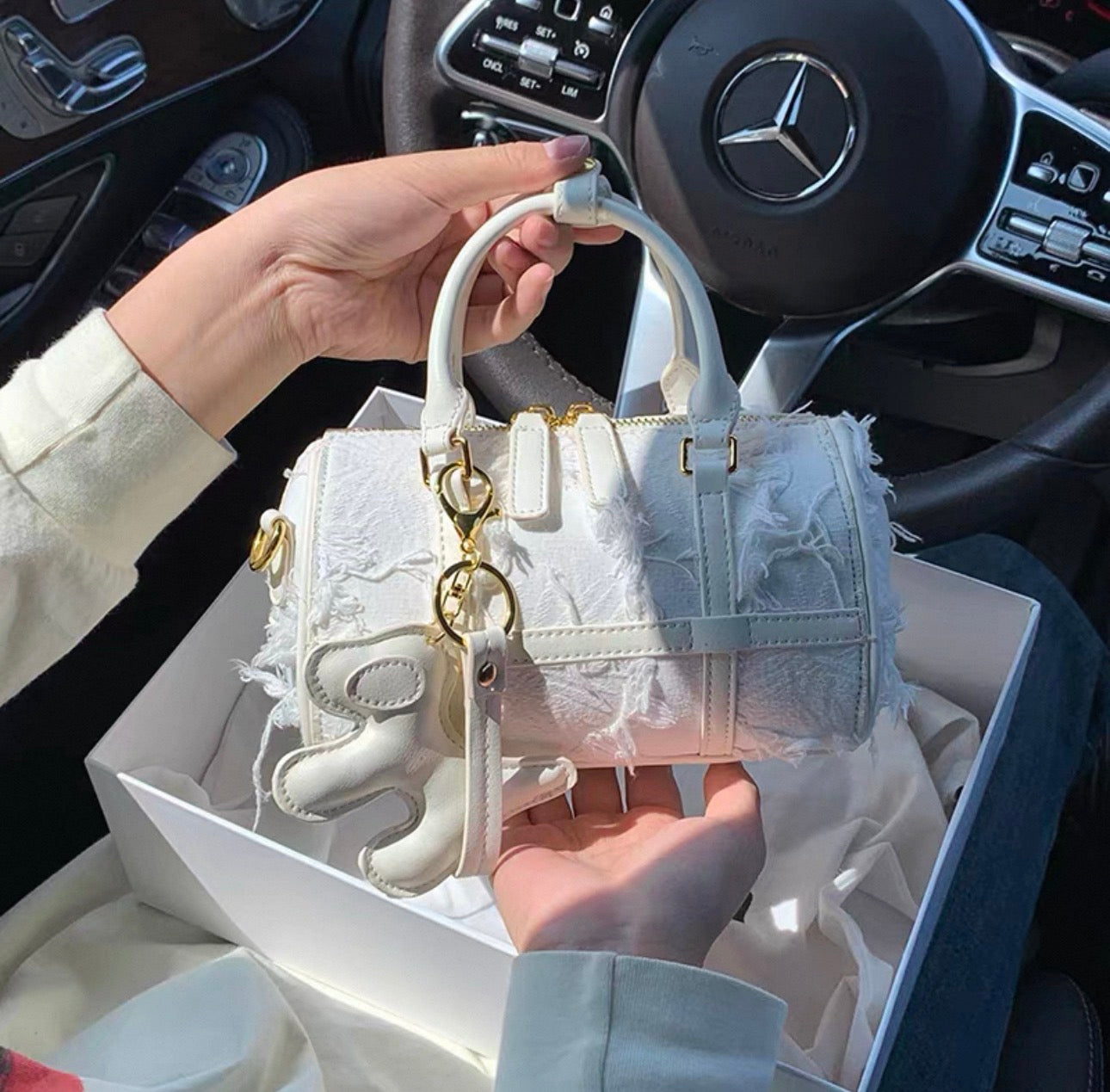 White Boston handbag with snowflake tassel charm and textured fabric detailing.