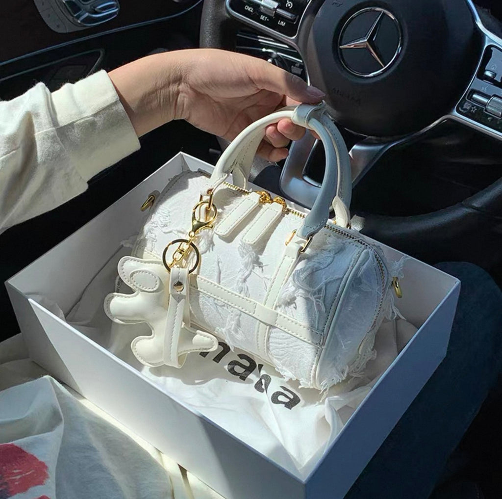 White Boston handbag with embossed snowflake pattern, gold hardware, and white tassel charm.