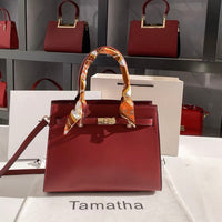 Red Kelly-style handbag with gold hardware and a patterned scarf wrapped around the handle.