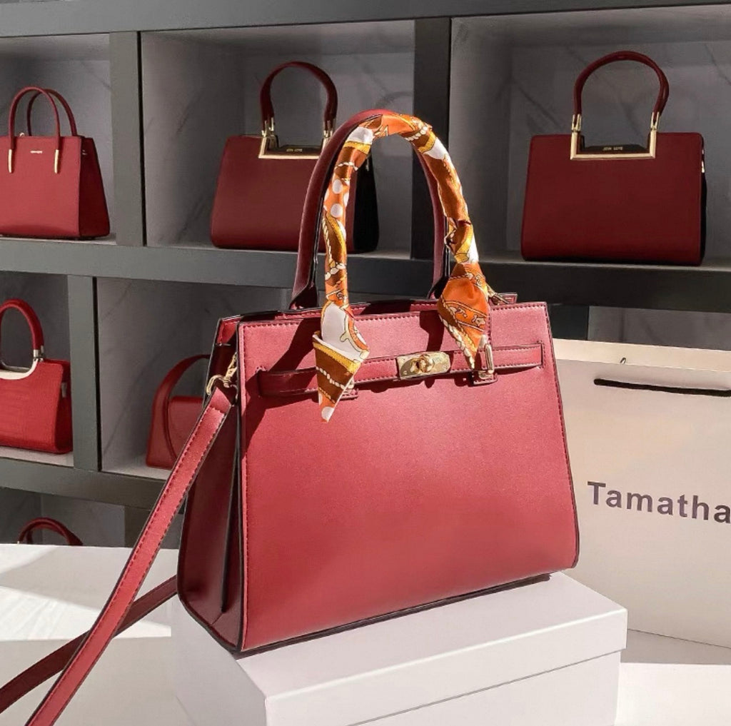 Red Kelly-style handbag with gold hardware and orange patterned scarf wrapped around handle.