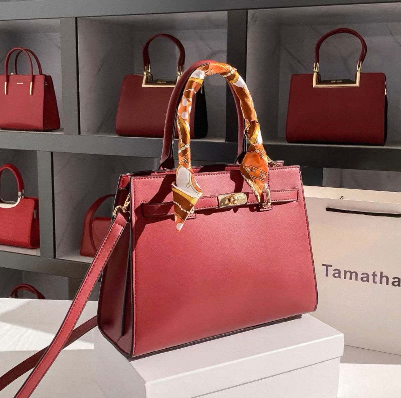 Red Kelly-style handbag with gold hardware and orange patterned scarf wrapped around handle.