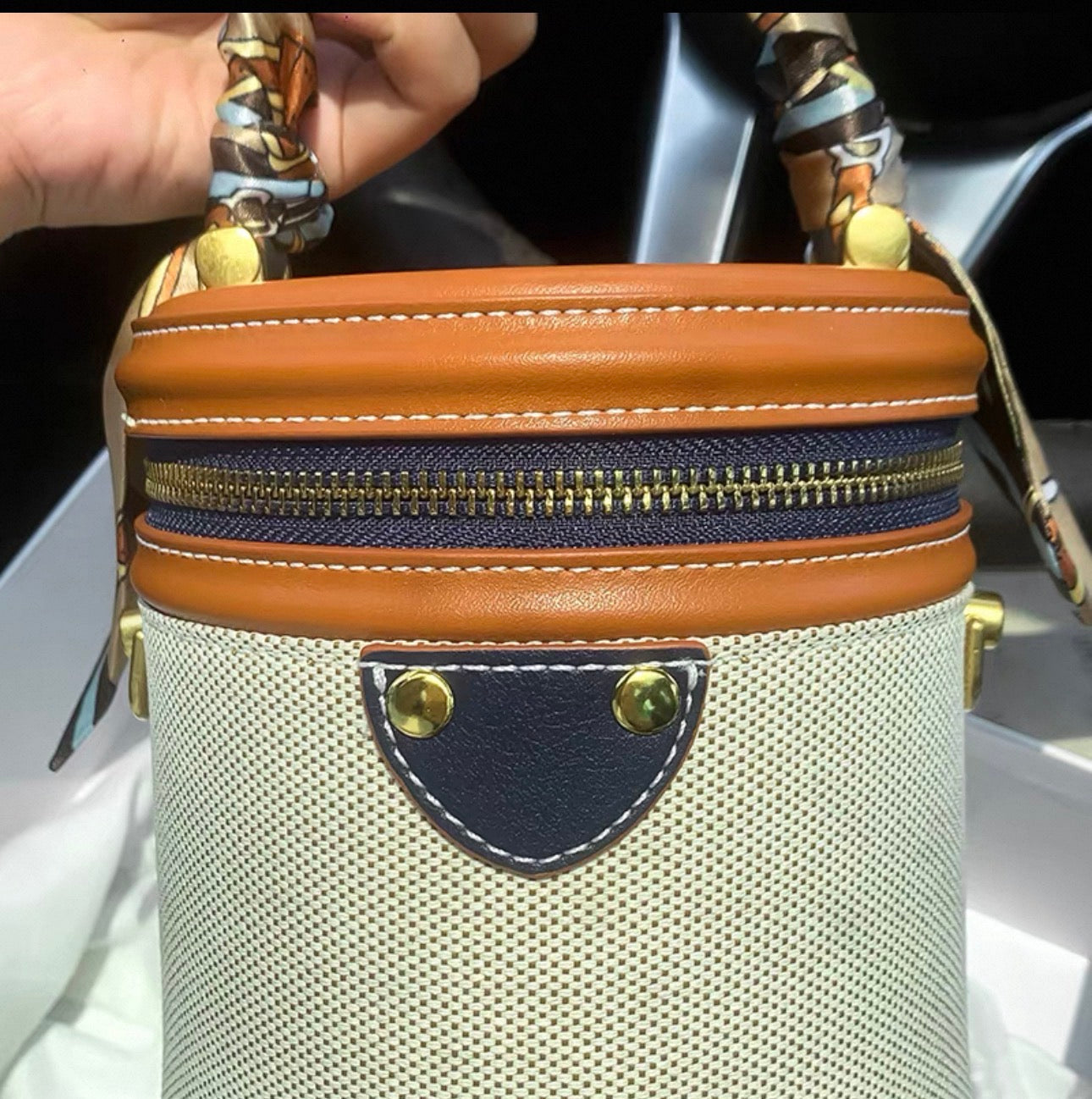 Cylindrical handbag with light brown, cream, and dark brown color-block panels, gold-tone zipper and hardware, and twisted.