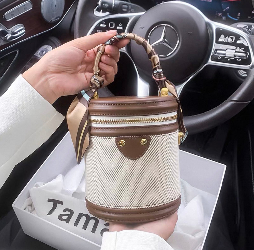 Multicolor cylindrical handbag with dark brown leather accents and a patterned handle strap.
