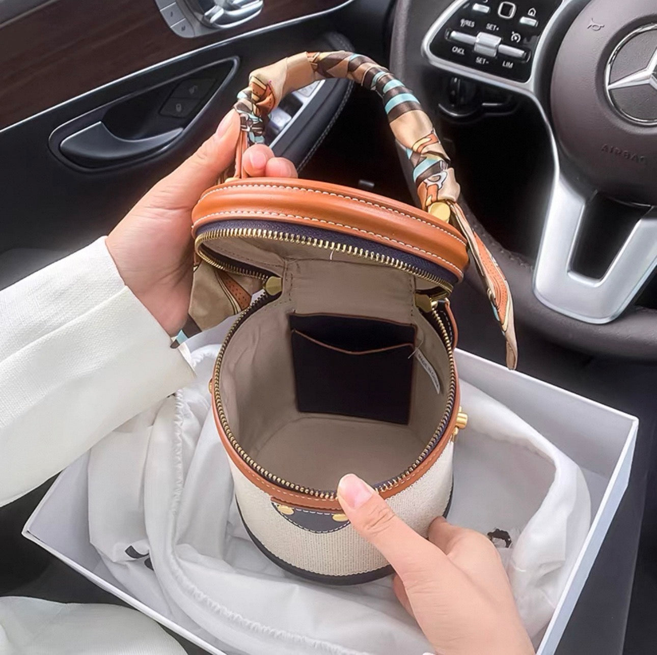 Multicolor cylindrical handbag with light brown top, beige body, and patterned handle, open with visible interior pocket.