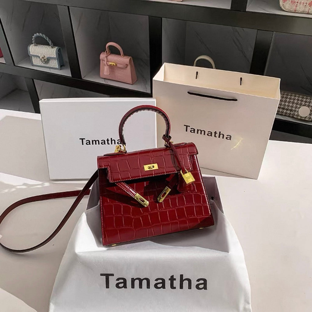 Ruby red Kelly-style handbag with glossy stone-pattern texture and gold lock hardware.
