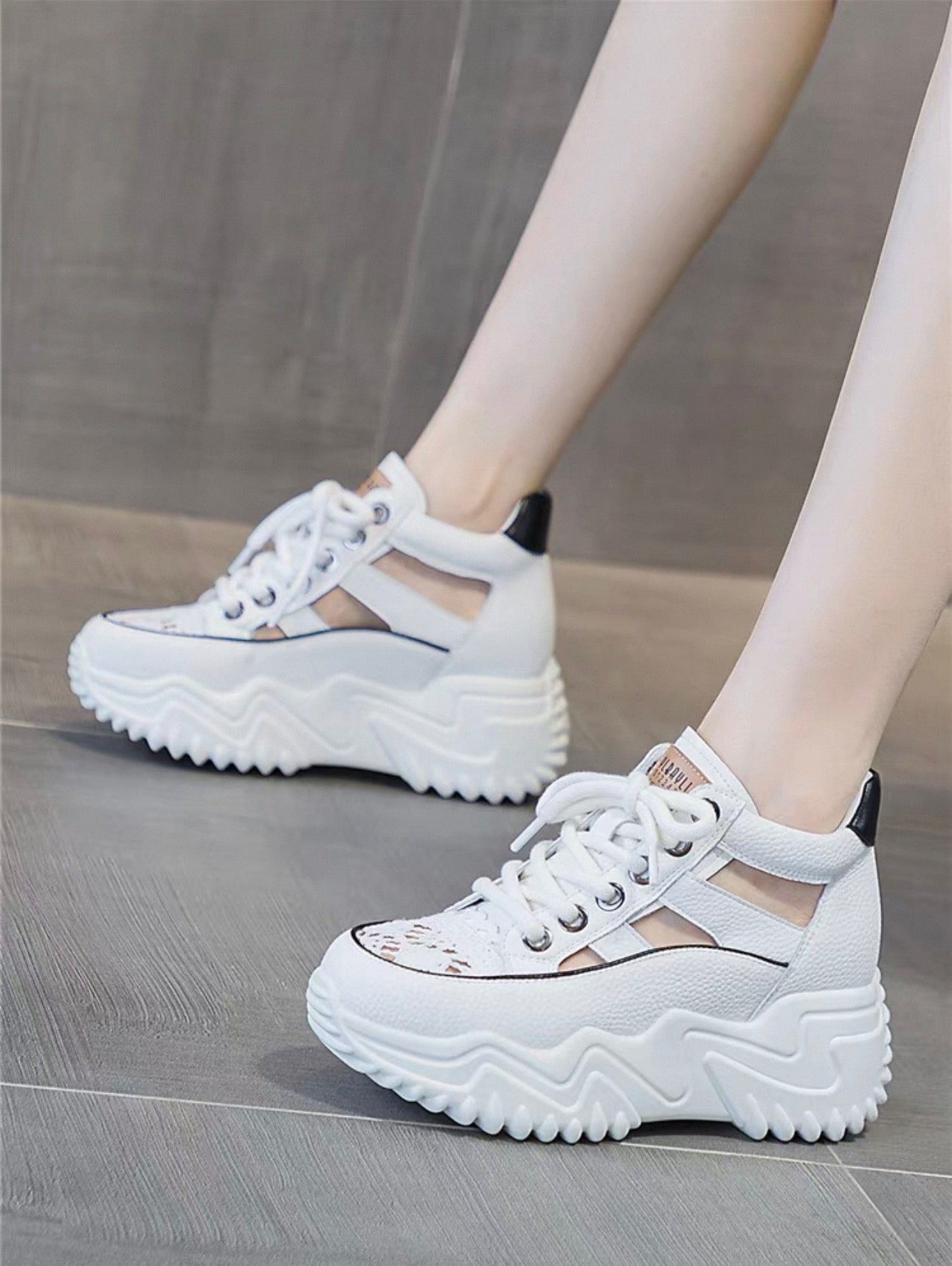White sneakers with thick soles worn by a person on a gray floor.