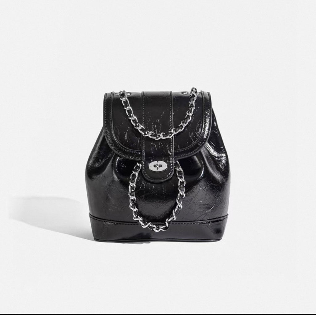 Black patent leather handbag with chain detail on a white background