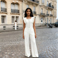 Woman in a white jumpsuit standing on a cobblestone street with a building in the background